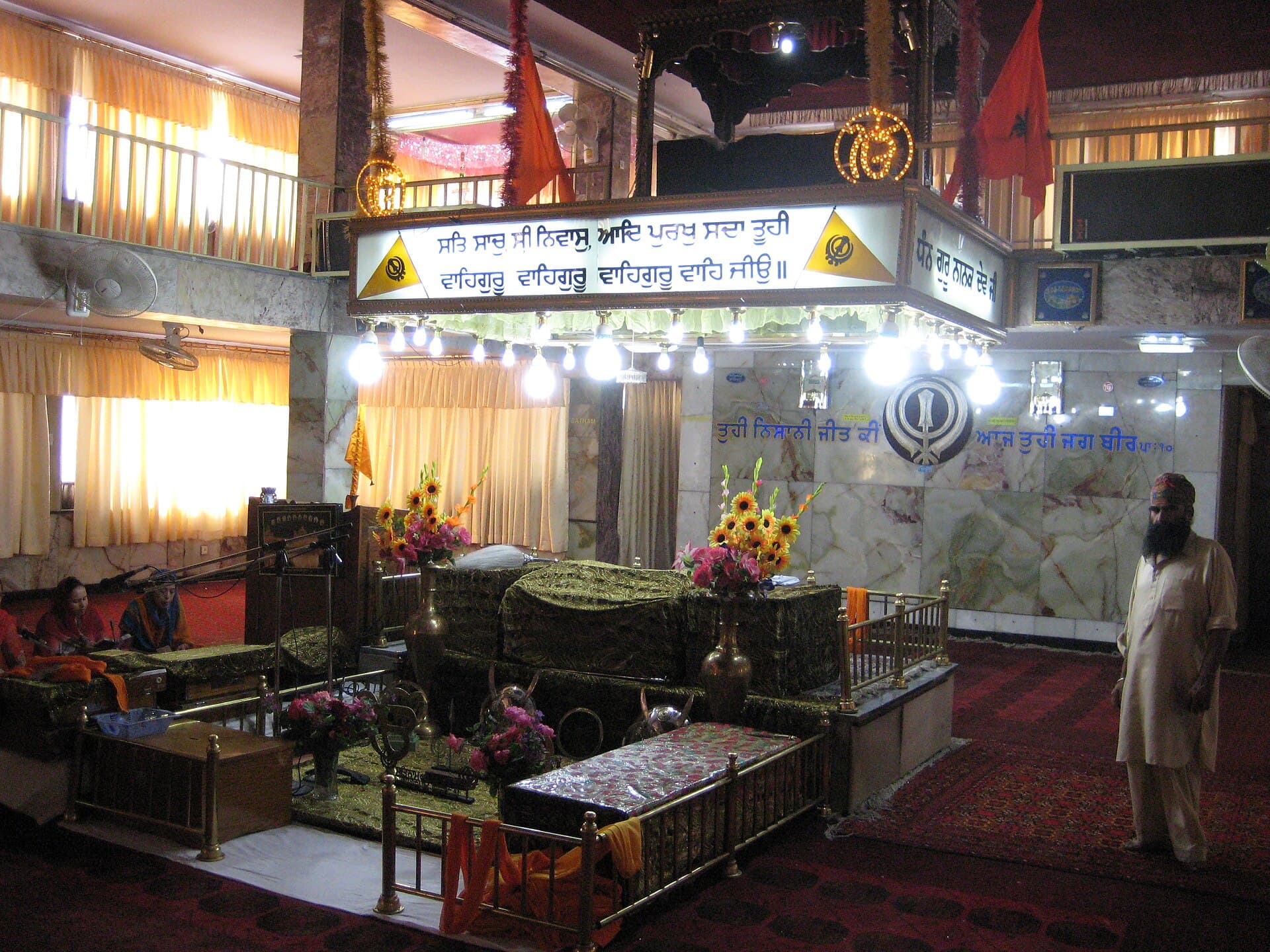 The darbar hall of Gurdwara Karte Parwan in Kabul, its Gurmukhi signage lit above the palki
